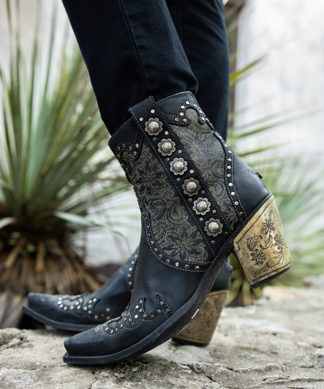 Black cowboy boots with intricate designs and embellishments on a stone surface.