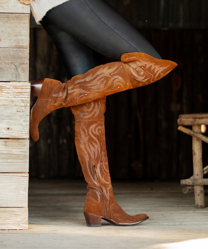 Brown cowboy boots with intricate stitching design worn by a person on a wooden porch.