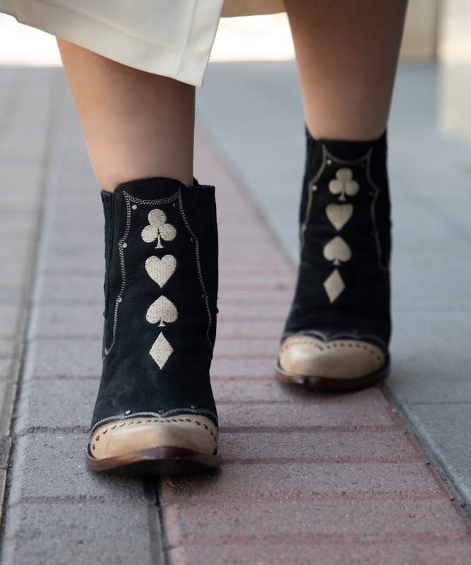 Black boots with stitching of card suit symbols worn on a pavement.